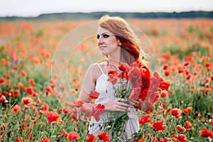 Beautiful young red-haired woman in poppy field holding a bouquet of poppies