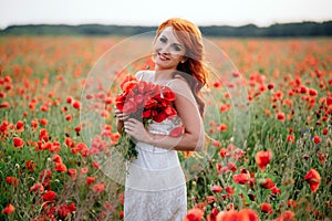 Beautiful young red-haired woman in poppy field holding a bouquet of poppies