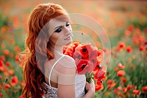 Beautiful young red-haired woman in poppy field holding a bouquet of poppies