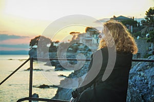 Beautiful young red-haired woman, at the seaside in the fishing village in Liguria, Italy enjoys the sunset
