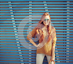 Beautiful young red-haired young girl in sunglasses standing near the wall of blue wooden planks summer warm day