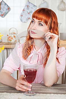 Beautiful young redhaired woman with glass of wine sitting in the kitchen