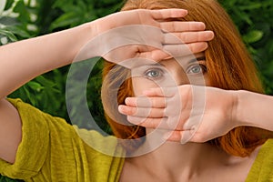 Beautiful young redhead woman hiding behind hands
