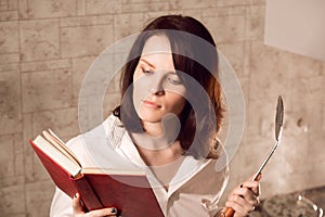 Beautiful young redhead woman reading a book while cooking on kitchen