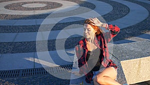 Beautiful young redheaded woman sitting on waterfront, enjoying nature and the good weather. The girl in red plaid shirt