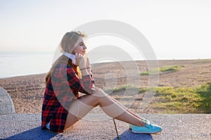 Beautiful young redheaded woman sitting on waterfront, enjoying nature and the good weather. The girl in red plaid shirt