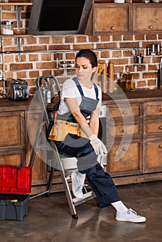 beautiful young repairwoman sitting on stepladder