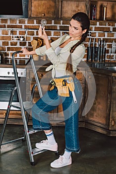 beautiful young repairwoman standing on stepladder and examining light bulb