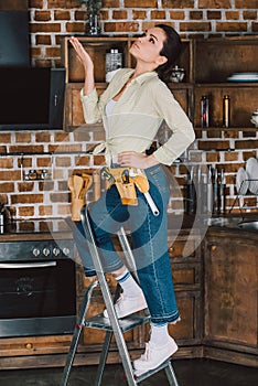 beautiful young repairwoman standing on stepladder at kitchen