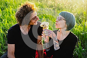 Beautiful young romantic couple on the field in summer. A woman blows on a fluffy dandelion flower. Flirting, romance, dating