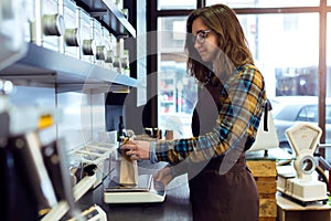 Beautiful young saleswoman weighing coffee beans in a retail store selling coffee. photo