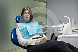 Beautiful young scared patient woman sitting in dental chair during examination at dental office looks frightened , healthcare