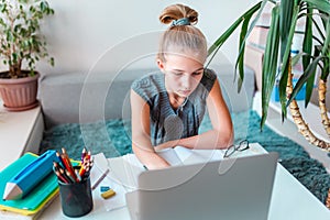 Beautiful young school girl left-handed working at home in her room with a laptop and class notes studying in a virtual class.