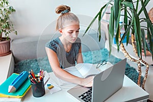 Beautiful young school girl left-handed working at home in her room with a laptop and class notes studying in a virtual class.