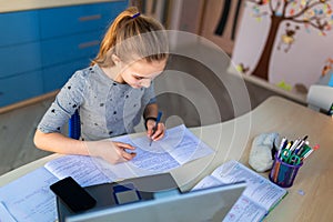 Beautiful young school girl working at home in her room with a laptop and class notes studying in a virtual class. Distance