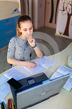 Beautiful young school girl working at home in her room with a laptop and class notes studying in a virtual class. Distance