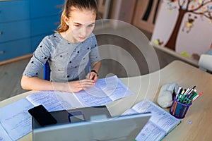 Beautiful young school girl working at home in her room with a laptop and class notes studying in a virtual class. Distance