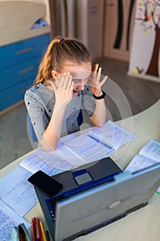 Beautiful young school girl working at home in her room with a laptop and class notes studying in a virtual class. Distance