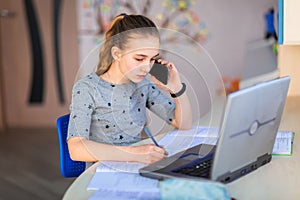 Beautiful young school girl working at home in her room with a laptop and class notes studying in a virtual class. Distance