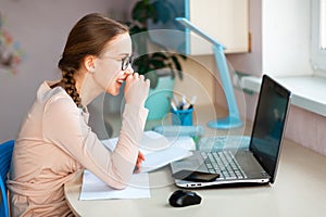 Beautiful young school girl working at home in her room with a laptop and class notes studying in a virtual class. Distance