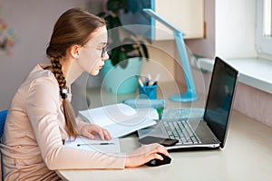 Beautiful young school girl working at home in her room with a laptop and class notes studying in a virtual class. Distance