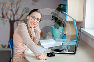Beautiful young school girl working at home in her room with a laptop and class notes studying in a virtual class. Distance