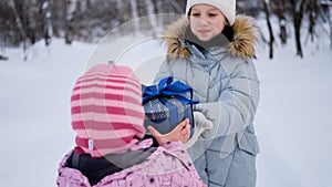 A beautiful young schoolgirl standing in a snowy forest in winter gives a gift to her little sister
