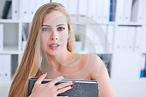 Beautiful young secretary hides her nakedness for a folder on an office background. Harassment concept.