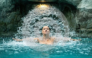 beautiful young sexy blonde naked woman portrait stretches arms, enjoying the rippling splashing water of the waterfall shower in