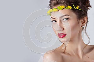 Beautiful young elegant woman with red lips, beautiful hair with a wreath of yellow roses on the head with bared shoulders