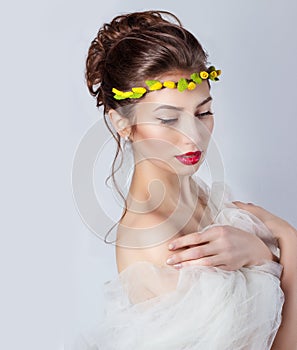 Beautiful young elegant woman with red lips, beautiful hair with a wreath of yellow roses on the head with bared shoulders