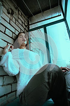 Beautiful young sexy girl posing on the balcony. Art photo portrait of a girl in a modern style with a sitting and added noise on