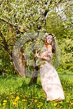 Beautiful young girl with red hair near flowering tree Apple orchard standing in a pink dress
