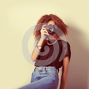 Beautiful young woman in jeans with a camera in the hands of curly hair in the Studio, retro filter