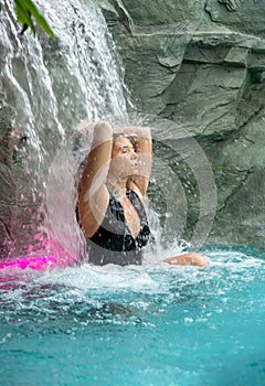 Beautiful young sexy woman with vitiligo disease in Bikini, enjoys the relaxation under the splashing water of the waterfall in
