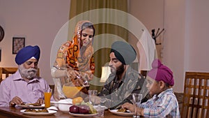 Beautiful young Sikh lady serving juice to her family members - family love. Indian army officer with his son, father, and wife