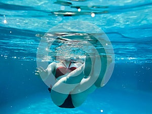 Beautiful young slender attractive girl, a woman in a red and black swimsuit swims, bathes under the blue water, underwater view o