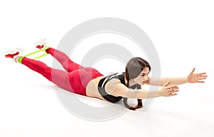 Beautiful, young, slender girl does sports exercises with a rubber expander on the floor, isolated on a white background