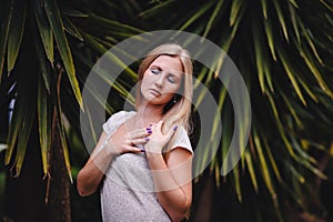 Beautiful, young, slender, long-haired blond girl in white long dress. A woman poses against the backdrop of palm trees and nature