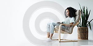 Beautiful young smiling african american woman working on laptop while sitting in bcomfortable chair at home