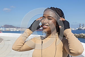 Beautiful young smiling afro american woman with headphones   with sea and sky background  boardwalk