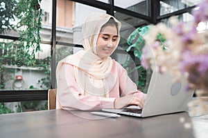 Beautiful young smiling asian muslim woman working on laptop sitting in living room at home.