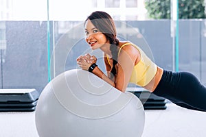 Beautiful young smiling Asian woman training pilates, yoga plank at gym with exercise ball