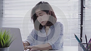 Beautiful young smiling asian woman working on laptop while sitting in a living room at home.