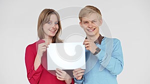 Beautiful young smiling couple looking at the camera and holding white poster