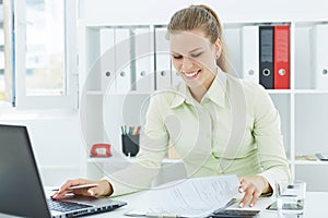 Beautiful young smiling secretary working with papers sitting at office.