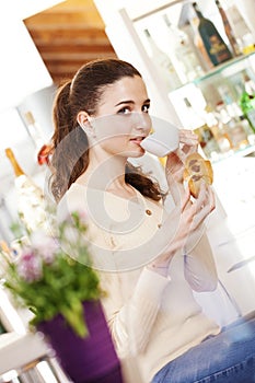 Beautiful young smiling woman with croissant and a cup of coffee in her hands at the cafe coffee bar, ice cream shop and pastry