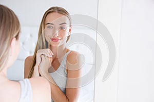 Beautiful young smiling woman,girl is touching her face while looking at the mirror.