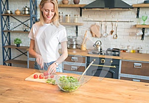 Beautiful young smiling woman making salad in the kitchen. Cutting tomatoes. Healthy food. vegetable salad. Diet. Healthy