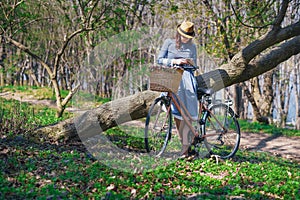 Beautiful young smiling woman with short dark hair and hat standing near bicycle with basket of huge bouquet of chamomiles.Summer